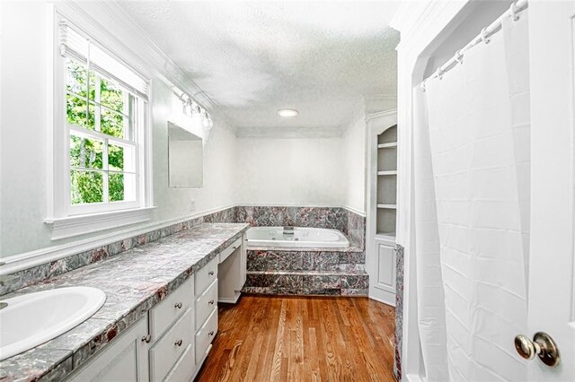 bathroom with a textured ceiling, vanity, hardwood / wood-style floors, and a relaxing tiled tub