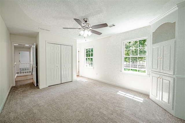 unfurnished bedroom with a closet, ceiling fan, light colored carpet, and a textured ceiling