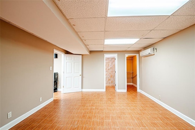 empty room with light hardwood / wood-style flooring, a drop ceiling, and a wall mounted AC