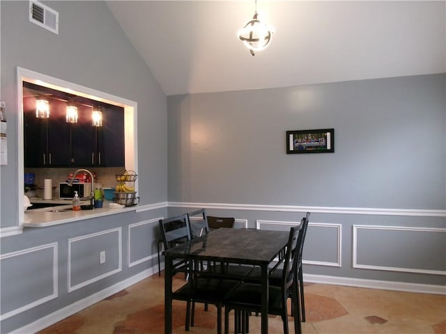 dining room with a wainscoted wall, visible vents, vaulted ceiling, and a decorative wall