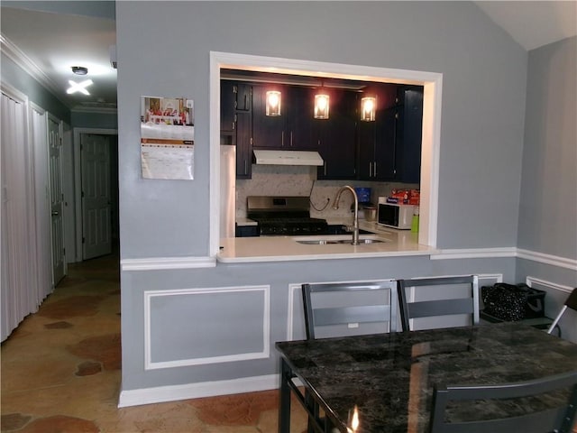 kitchen with decorative backsplash, gas stove, vaulted ceiling, a sink, and under cabinet range hood