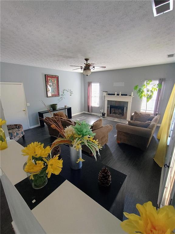 living room featuring ceiling fan, a tiled fireplace, a textured ceiling, and a wealth of natural light