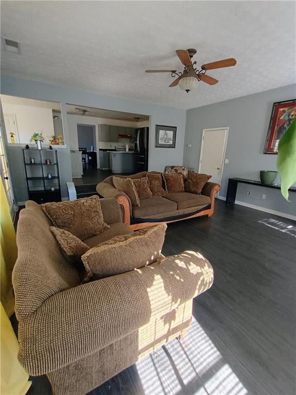 living room with ceiling fan, dark wood-type flooring, and a textured ceiling