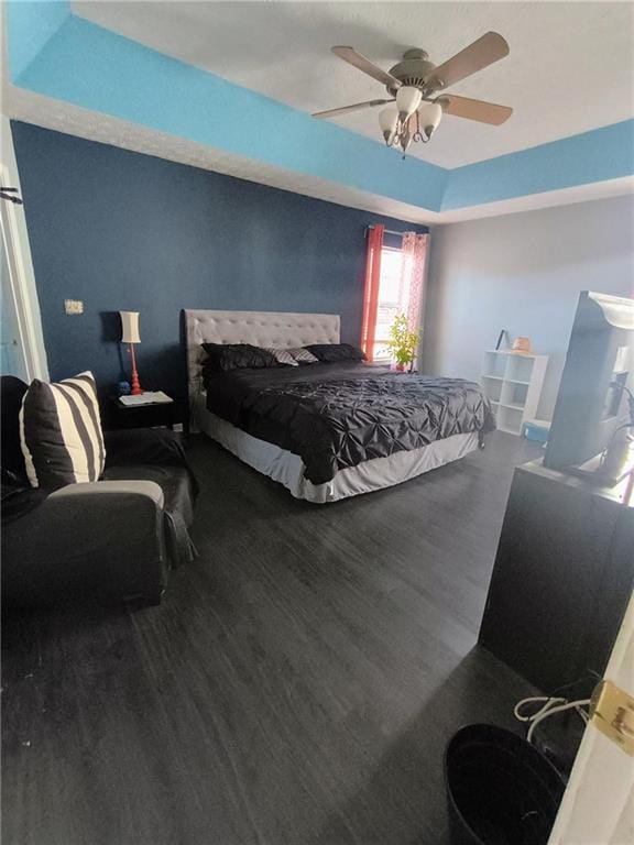 bedroom with a raised ceiling, hardwood / wood-style flooring, and ceiling fan