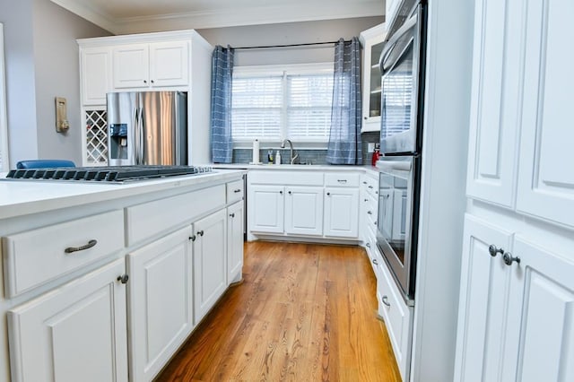 kitchen with appliances with stainless steel finishes, sink, white cabinets, crown molding, and light hardwood / wood-style flooring