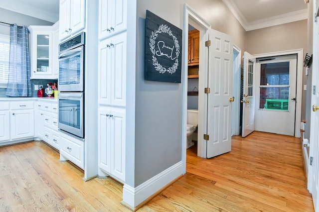 kitchen with white cabinetry, stainless steel double oven, light hardwood / wood-style floors, and backsplash