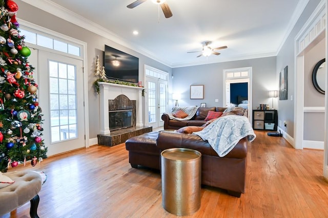 living room with a tile fireplace, ornamental molding, ceiling fan, and light hardwood / wood-style flooring