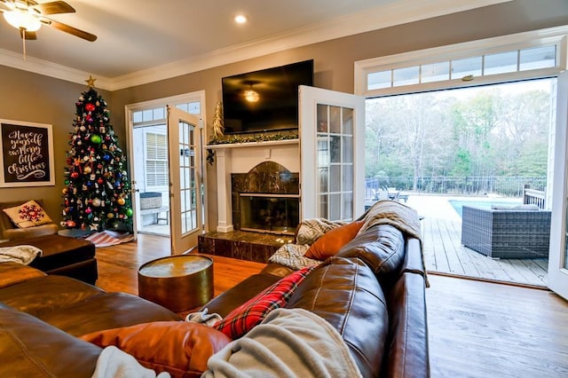 living room with french doors, wood-type flooring, ornamental molding, ceiling fan, and a fireplace