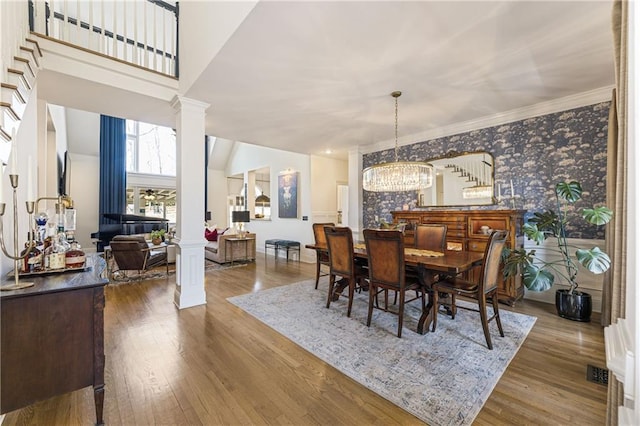 dining area featuring visible vents, wood finished floors, wallpapered walls, decorative columns, and a chandelier