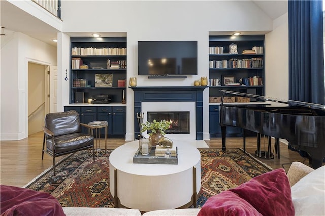 living room with built in shelves, baseboards, a fireplace with flush hearth, wood finished floors, and high vaulted ceiling