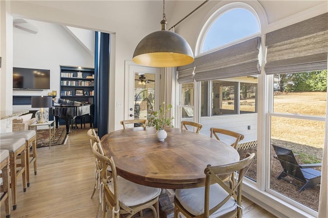 dining space with light wood-style flooring, a ceiling fan, a towering ceiling, and a sunroom