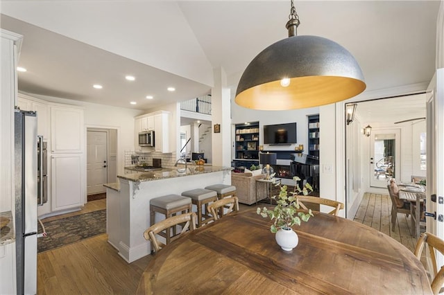 dining space featuring dark wood finished floors, recessed lighting, a warm lit fireplace, and vaulted ceiling