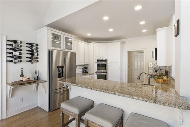 kitchen featuring tasteful backsplash, appliances with stainless steel finishes, a peninsula, and light stone countertops