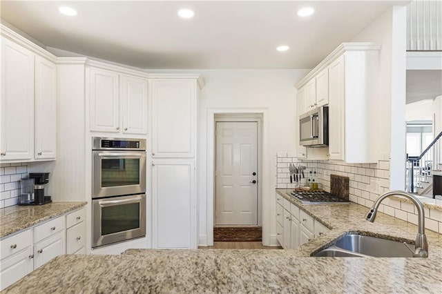 kitchen with a sink, light stone counters, appliances with stainless steel finishes, and white cabinets