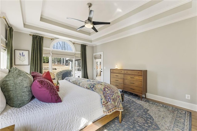 bedroom with a raised ceiling, ornamental molding, wood finished floors, baseboards, and ceiling fan