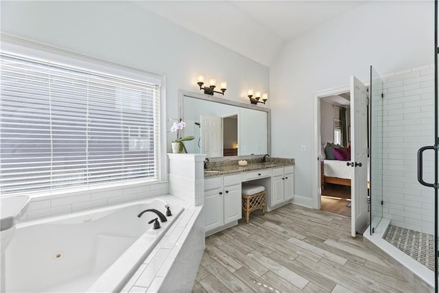 ensuite bathroom featuring a sink, a jetted tub, connected bathroom, double vanity, and vaulted ceiling