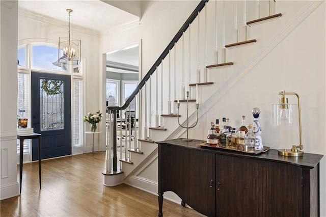 entryway featuring stairs, ornamental molding, an inviting chandelier, wood finished floors, and a bar