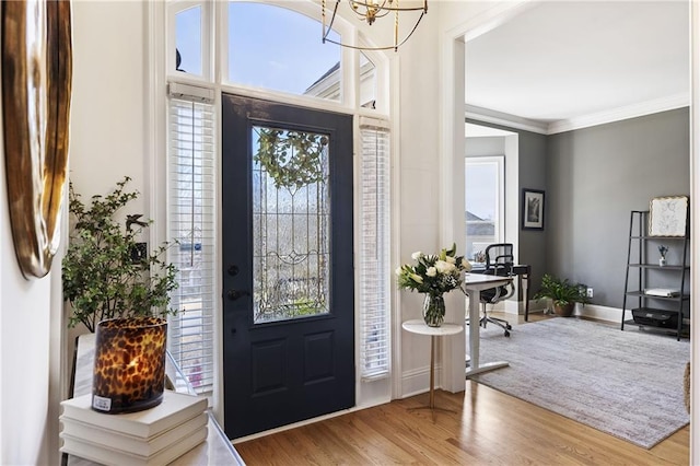 foyer featuring an inviting chandelier, wood finished floors, baseboards, and ornamental molding