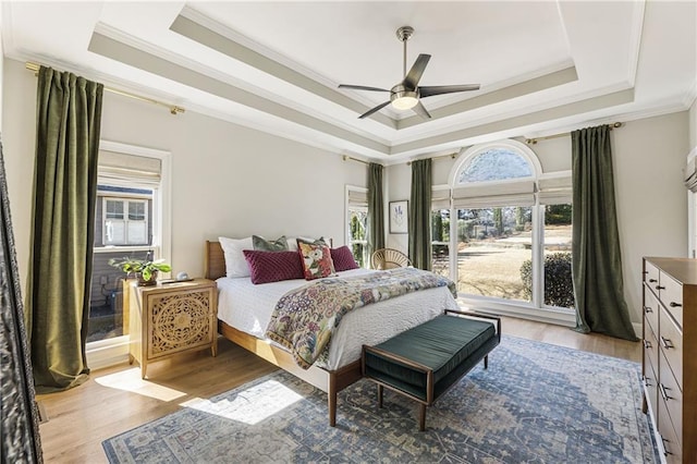 bedroom featuring light wood-style flooring, a raised ceiling, ceiling fan, and ornamental molding