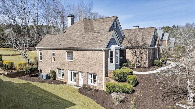 rear view of property with central AC unit, fence, a chimney, a lawn, and brick siding