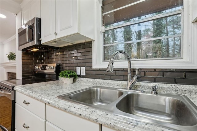 kitchen with backsplash, light stone counters, white cabinets, stainless steel appliances, and a sink