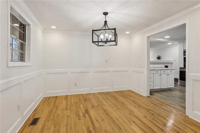 unfurnished dining area with visible vents, ornamental molding, a textured ceiling, light wood-style floors, and an inviting chandelier