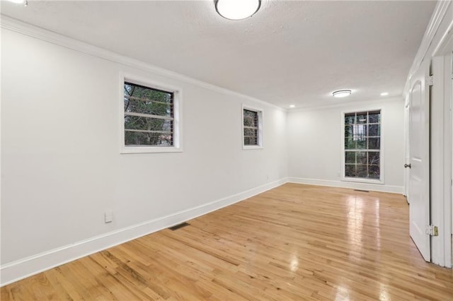 empty room with crown molding, light wood-style floors, and baseboards