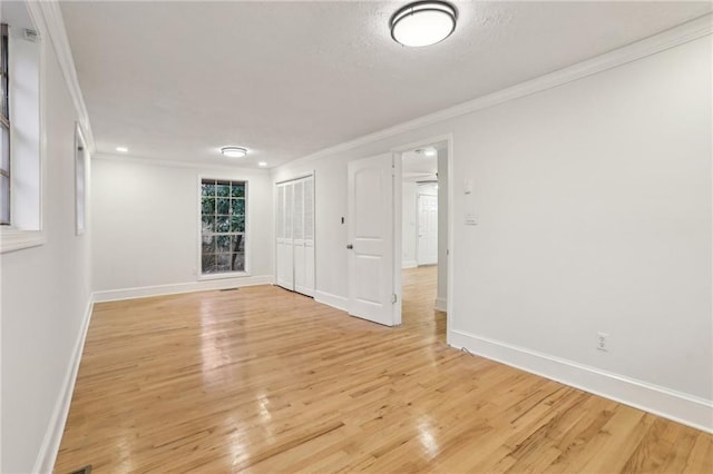 empty room featuring a textured ceiling, baseboards, light wood-style floors, and ornamental molding