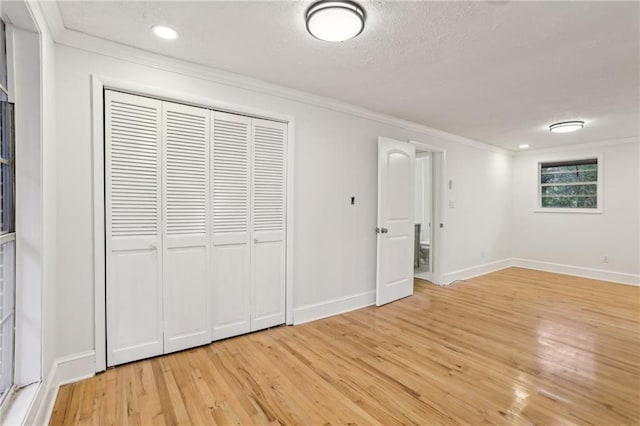 unfurnished bedroom with a textured ceiling, baseboards, light wood finished floors, and ornamental molding