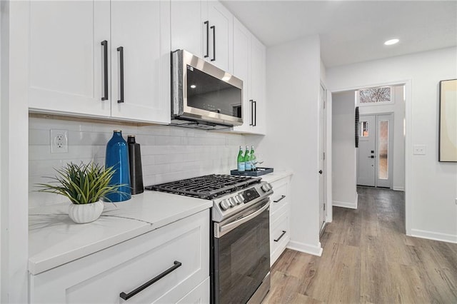 kitchen with tasteful backsplash, white cabinetry, light stone counters, stainless steel appliances, and light hardwood / wood-style flooring