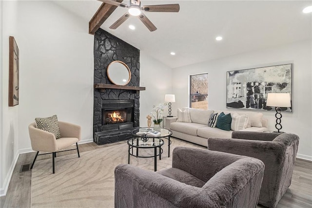 living room with vaulted ceiling with beams, a stone fireplace, light hardwood / wood-style floors, and ceiling fan