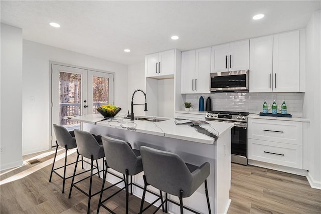 kitchen with sink, appliances with stainless steel finishes, an island with sink, white cabinets, and french doors