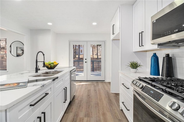 kitchen featuring stainless steel appliances, white cabinetry, sink, and light stone counters