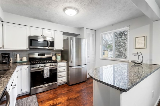 kitchen with dark stone countertops, backsplash, white cabinetry, stainless steel appliances, and dark wood-style flooring