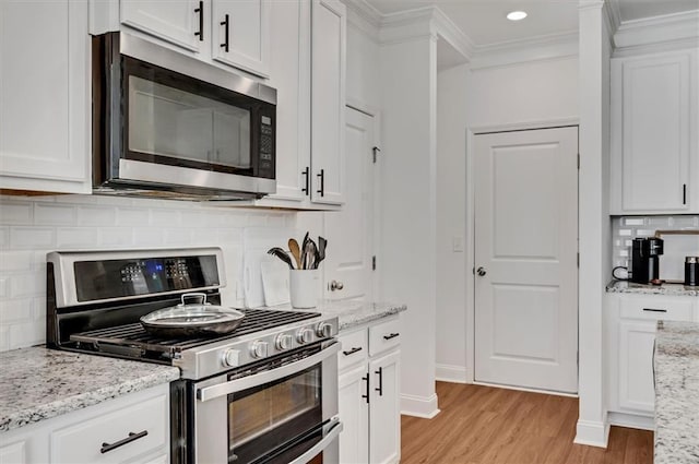 kitchen featuring white cabinets, light stone counters, stainless steel appliances, crown molding, and light wood-type flooring