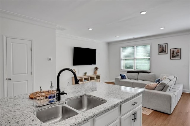 kitchen featuring sink, white cabinetry, light stone counters, ornamental molding, and light wood-type flooring