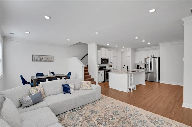 living room with crown molding, sink, and light hardwood / wood-style flooring