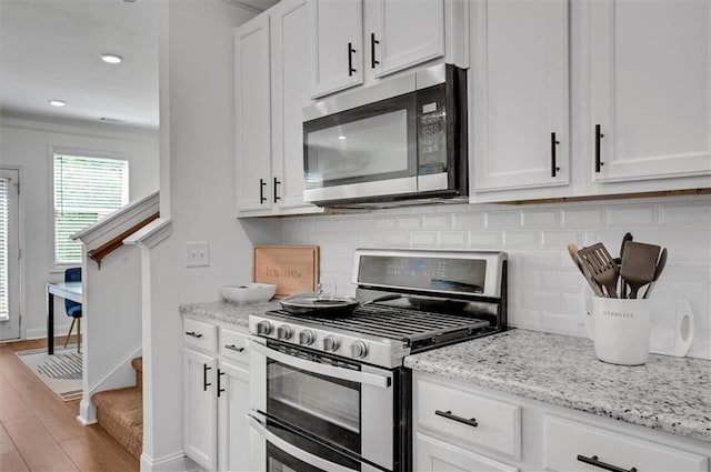 kitchen featuring light stone counters, light hardwood / wood-style flooring, white cabinets, stainless steel appliances, and backsplash