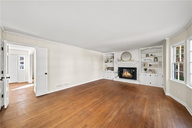 unfurnished living room featuring visible vents, hardwood / wood-style flooring, ornamental molding, built in shelves, and a fireplace