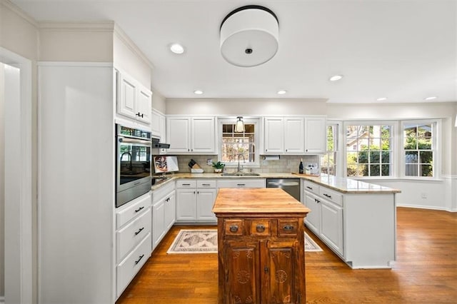 kitchen with stainless steel appliances, wood finished floors, a kitchen island, white cabinetry, and decorative backsplash