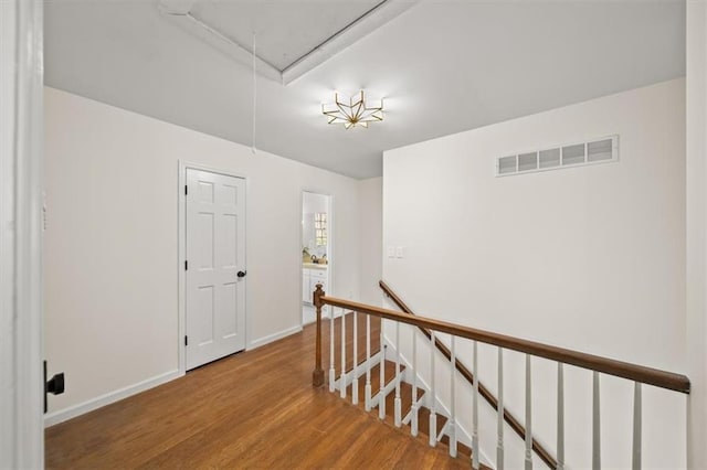 hallway featuring attic access, baseboards, visible vents, wood finished floors, and an upstairs landing