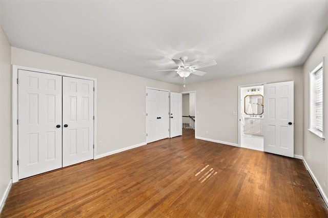 unfurnished bedroom with baseboards, dark wood-style flooring, connected bathroom, and multiple closets