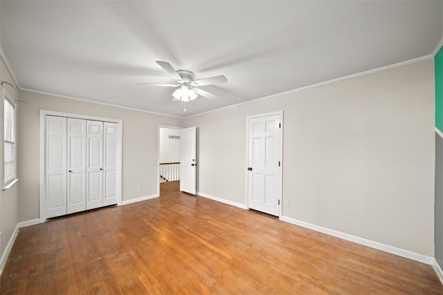 unfurnished bedroom with ceiling fan, wood finished floors, baseboards, ornamental molding, and a closet