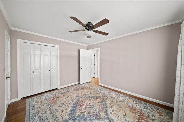 unfurnished bedroom with baseboards, a ceiling fan, ornamental molding, wood finished floors, and a closet