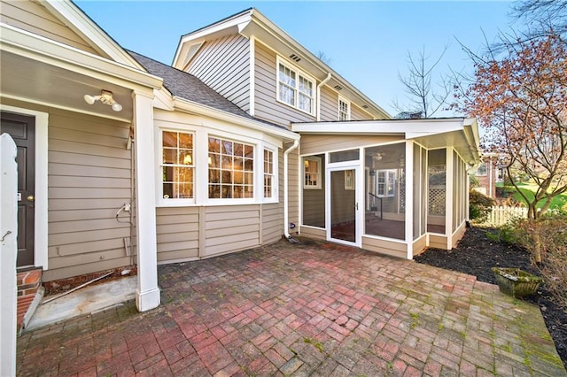 rear view of property with a sunroom, roof with shingles, fence, and a patio