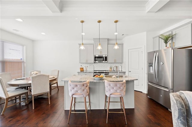 kitchen with pendant lighting, beam ceiling, a kitchen island with sink, and appliances with stainless steel finishes