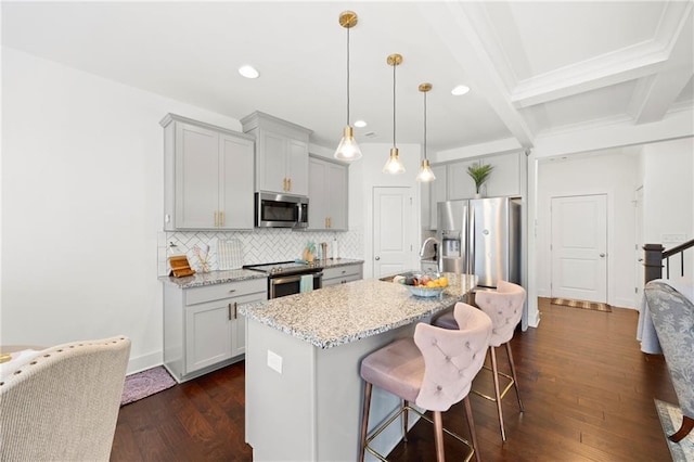 kitchen with light stone countertops, appliances with stainless steel finishes, beam ceiling, a center island with sink, and a breakfast bar area