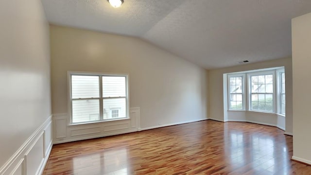 unfurnished room featuring a textured ceiling, vaulted ceiling, and light wood-type flooring