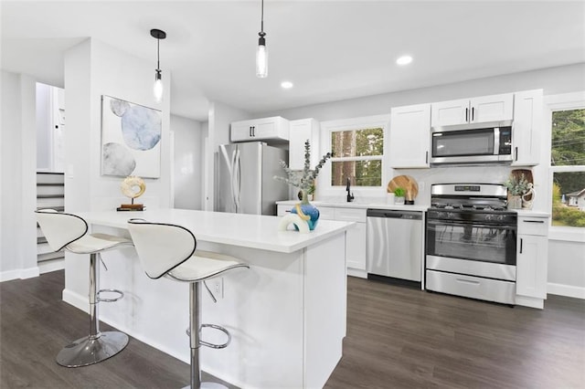 kitchen with appliances with stainless steel finishes, decorative light fixtures, white cabinetry, and a breakfast bar area