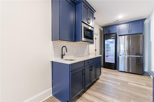 kitchen with blue cabinets, tasteful backsplash, sink, stainless steel fridge, and light hardwood / wood-style floors